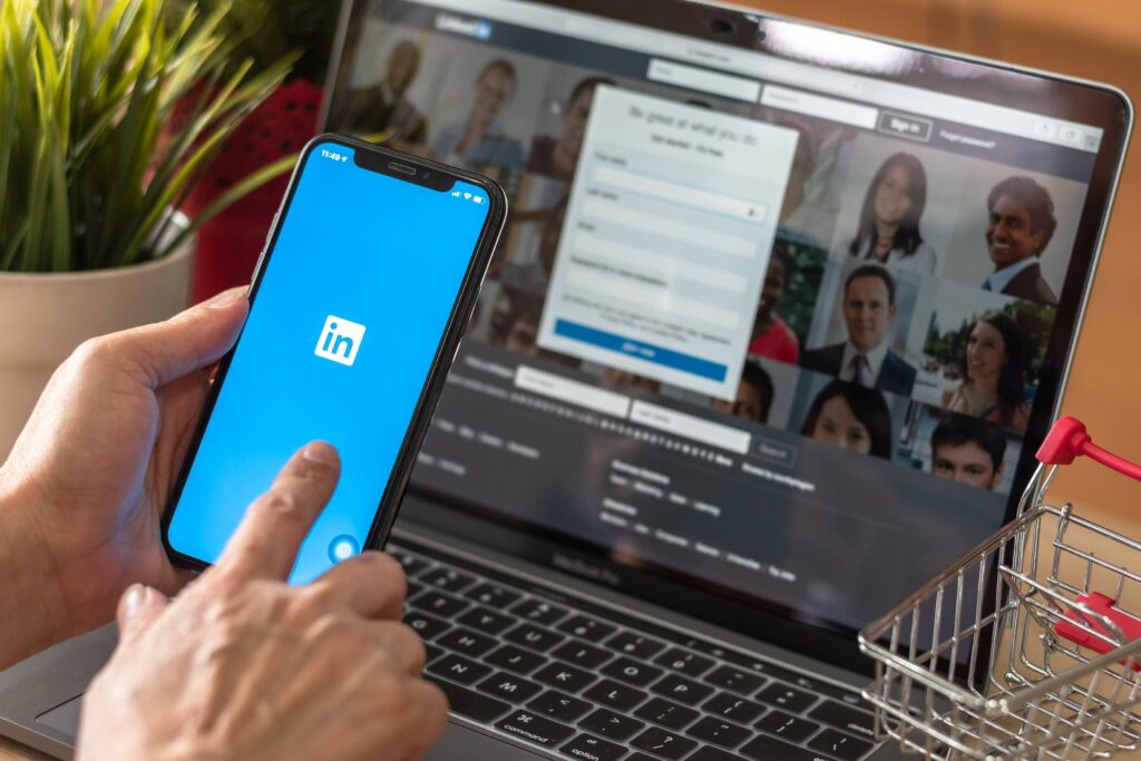 Smartphone displaying LinkedIn app next to a laptop showing professional profiles